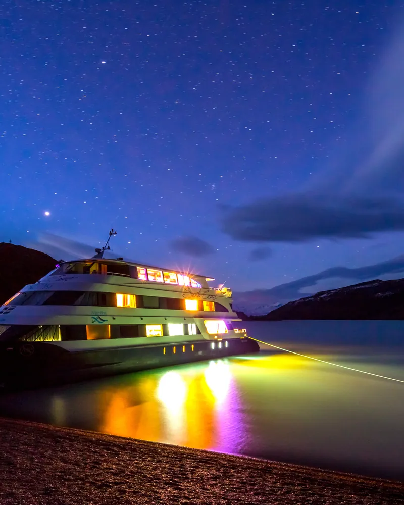 Crucero iluminado bajo el cielo nocturno junto a las aguas del Lago Argentino